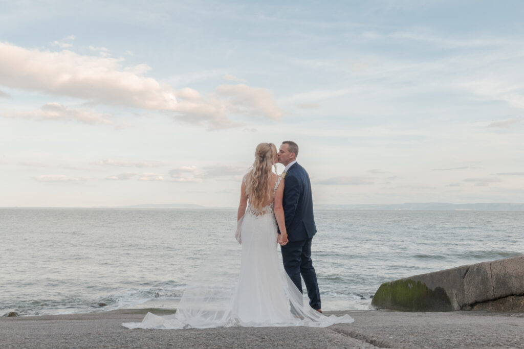 Couples kiss with the blue sea in the background on their wedding day